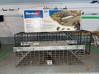 Photo showing two Havahart live animal cage traps side by side with the Havahart box on top. The traps have wire mesh construction with visible rust and metal plates with handles.