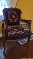 Front angled view of the needlepoint armchair showing burgundy floral upholstery and wooden frame.