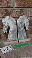 Full view of two marble horse head bookends, one with detached base, against brick background.