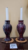 Pair of red marble candle holders with white taper candles on handmade wood coasters, front view.