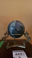 Full view of the marble sphere held by the brass dragon stand on a wooden surface.