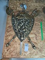 Full view of the medieval style shield and attached crossed weapons including two swords and two axes on wooden board