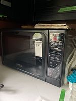 Black Panasonic Dimension 4 Genius Inverter microwave on a white counter with some papers on top, viewed from left front angle showing door and control panel.