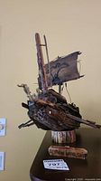 Front side view of the handmade wooden Roman war ship with a fabric sail and oars on a wooden stand.