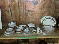 Full display of the china set showing various plates, bowls, covered bowls, cups, saucers, gravy boat, and platters arranged on a workbench shelf.