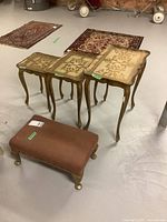 Photo showing three ornate nesting tables and one upholstered foot stool in basement