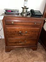 Front view of one nightstand showing three drawers and brass hardware