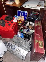 Photo showing Panasonic fax machine, red ladybug storage cube, red briefcase, assorted writing and office supplies