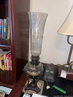 Bronze oil lamp with etched glass chimney on a tripod bronze base beside bookshelf and lamp