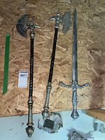 Photo showing three medieval replica weapons: two axes and one sword laid flat on a plywood surface.