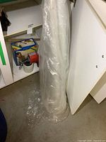 Partial roll of clear plastic drop sheet shown vertically rolled and leaning against a wall.