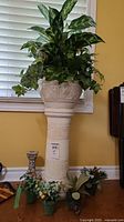 Full view of white ceramic plant pedestal with matching pot containing faux foliage and four small faux flower arrangements positioned around base