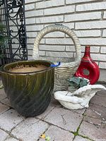 Lot items arranged on paved outdoor area: concrete basket planter, large glazed green planter, red vase, white swan garden ornament.
