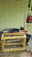 Wide view showing handmade wooden potting table in front of various resin planters of different sizes and colors against brick wall.