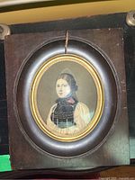 Framed vintage portrait showing woman in historical dress inside oval gold-trimmed glass frame with large crack on wood frame at the top.