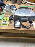 Photo showing all items in the lot placed on wooden surface including Panasonic CD radio, Misakai cassette radio, Sanyo cassette recorder, phone, headset, and power adapter.