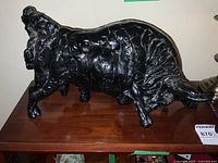 Front and side view of the large black bull sculpture on a wooden surface, showing its textured body and stance.