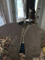 Front view of a brown mens Rainforest coat with zipper, large pockets and corduroy collar, displayed on a floral patterned chair.