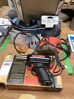Photo showing Weller soldering iron atop its box with power cord coiled and a small container of Kester solder nearby along with red Mini Max corner sander and various sandpaper sheets in the background.