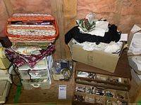 Wider view of the lot showing the plastic organizer with drawers, fabric pieces, woven basket, sewing box, and cardboard box with lace pieces.