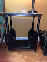 Side view of the black Bombay style side table showing the magazine storage compartments on both sides and the turned leg design.