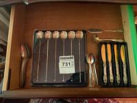 Photo of the utensils arranged in a drawer showing six swizzle spoons with shell ends, butter spreader, teaspoons, and extra spoon.