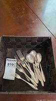 Silverplated spoons and forks placed in a black basket showing overall set and quantity.