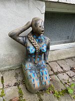 Front view of kneeling woman statue showing geometric paint patterns on chest and thighs, braided hair sculpted down front, some wear.