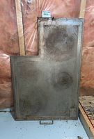 Front view of heavy metal stove top cover showing shape, discoloration, and handle.