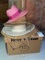 Five straw hats stacked on a box, pink hat on top, natural tones below