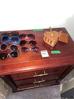 Seven pairs of assorted sunglasses and two wooden keepsake boxes displayed on a wooden dresser