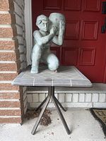 Person holding pot garden statue on tile-top table in front of red door.