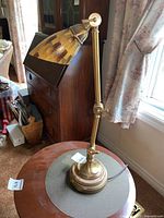 Full view of brass lamp on round stone base with adjustable arm and mosaic glass shade, items visible in background