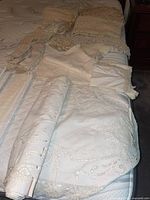 Wide view of the collection of linens showing layers of folded tablecloths, runners and doilies with lace and embroidery details.