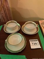 Three small teacups with matching saucers displayed on a table under warm lighting.