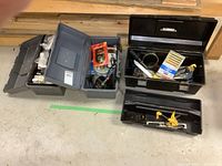 Three plastic toolboxes open showing assorted tools and hardware items inside.