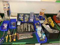 Image showing multiple hand tools including vise grips, pliers, screwdriver, and accessories laid out on a green surface with various plastic bins holding hardware parts and screws.