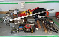 Wide view of assorted hand tools, measuring tape, protective goggles, hammer, mallet, screwdrivers, wire, and more arranged on a workbench surface under a wall socket.
