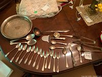 Photo showing full assortment of silver plated spoon types, ladles, cheese slicer, and serving tray on table.