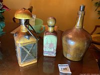 Three glass liquor bottles covered in leather shown together on a table, distinct shapes and stoppers visible