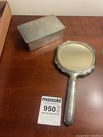 Photo showing hand held vanity mirror and hammered metal box on wooden surface