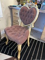 Front and side view of vanity chair showing heart-shaped tufted backrest, tufted seat, antique finish wood frame, carved details and curved legs.