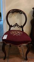 Front view of Victorian wooden chair with rounded, ornately carved backrest and needlepoint upholstered seat.