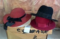 Three wool felt hats on a storage box, two visible (red and black with bands) and one white vintage dress hat mentioned in description but not clearly shown.