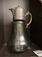 Full view of the smoke glass pitcher with metal ornate handle and lid, showing the glass body and the attached metal lid with finial knob