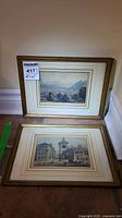 Two framed prints leaning against a wall, showing the front with landscape scenes and wood frames.