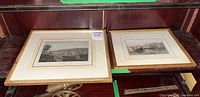 Two framed vintage prints seen side by side on a wooden surface, showing cityscapes with gold-tone frames and white matting.