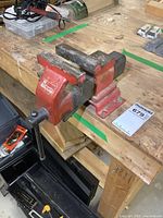 Side view of the Record 4 bench vise mounted on a wooden workbench, showing its red body and black jaws with some surface rust.