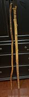 Full length view of two carved wooden walking sticks leaning against a black cabinet