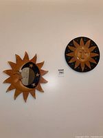 Two wooden sun wall art pieces mounted on wall; one has a sun face with black and yellow paint, other has crescent moon mirror with stars on a wooden sun frame.